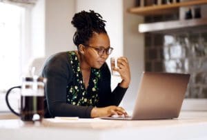 Shot of a young african american woman with a coffee cup using laptop in kitchen at home